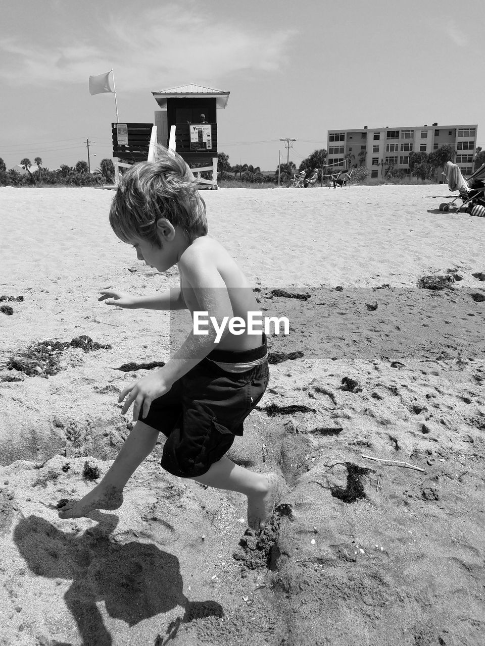 Side view of shirtless playful boy jumping at sandy beach on sunny day