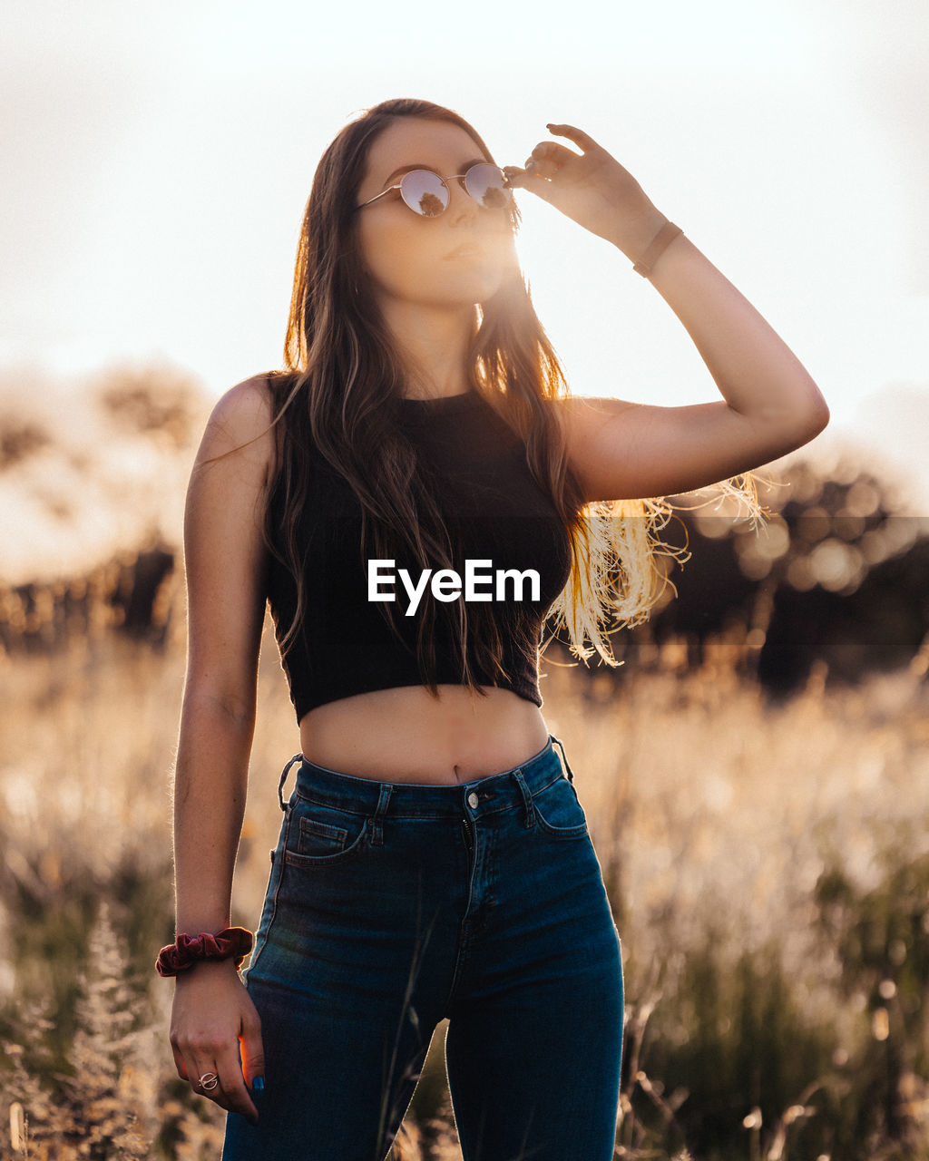 Young woman with sunglasses standing on field against sky