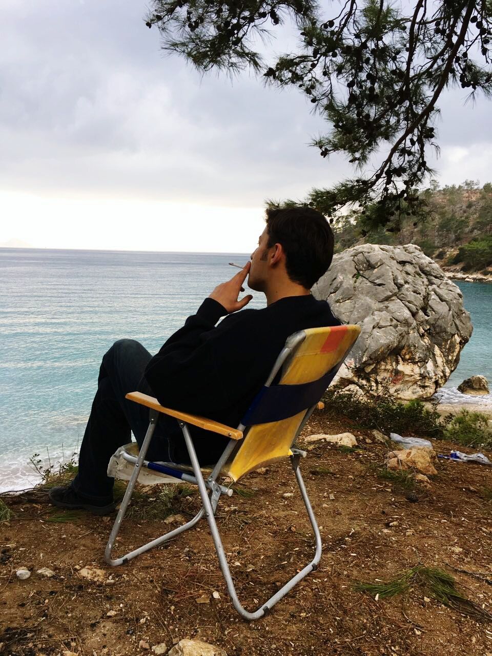 Man smoking cigarette while sitting on chair at beach