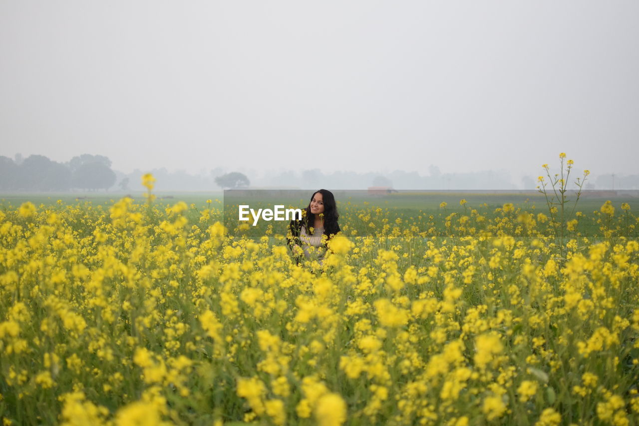 Portrait of young woman amidst yellow flowers on oilseed rape field