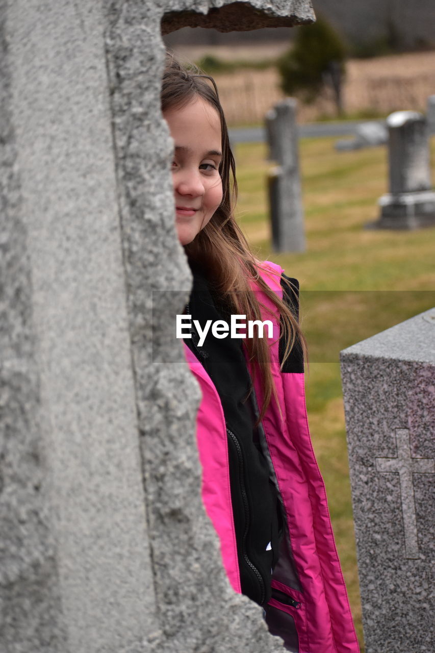 Portrait of smiling girl standing by cross in cemetery