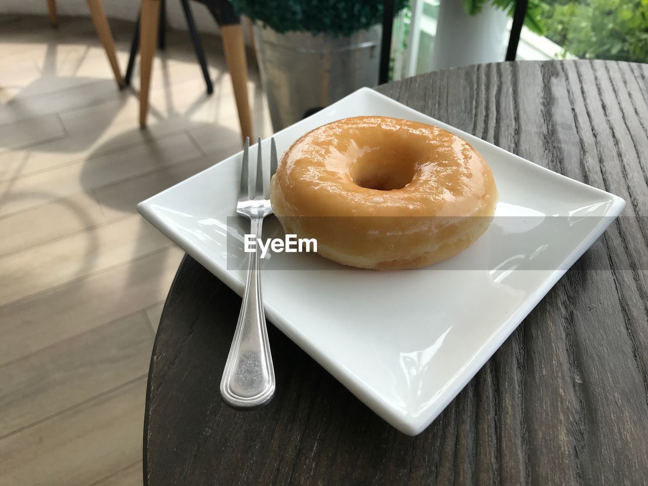 A delightful sugar glazed donut served on a white plate on a wooden table in a coffee shop