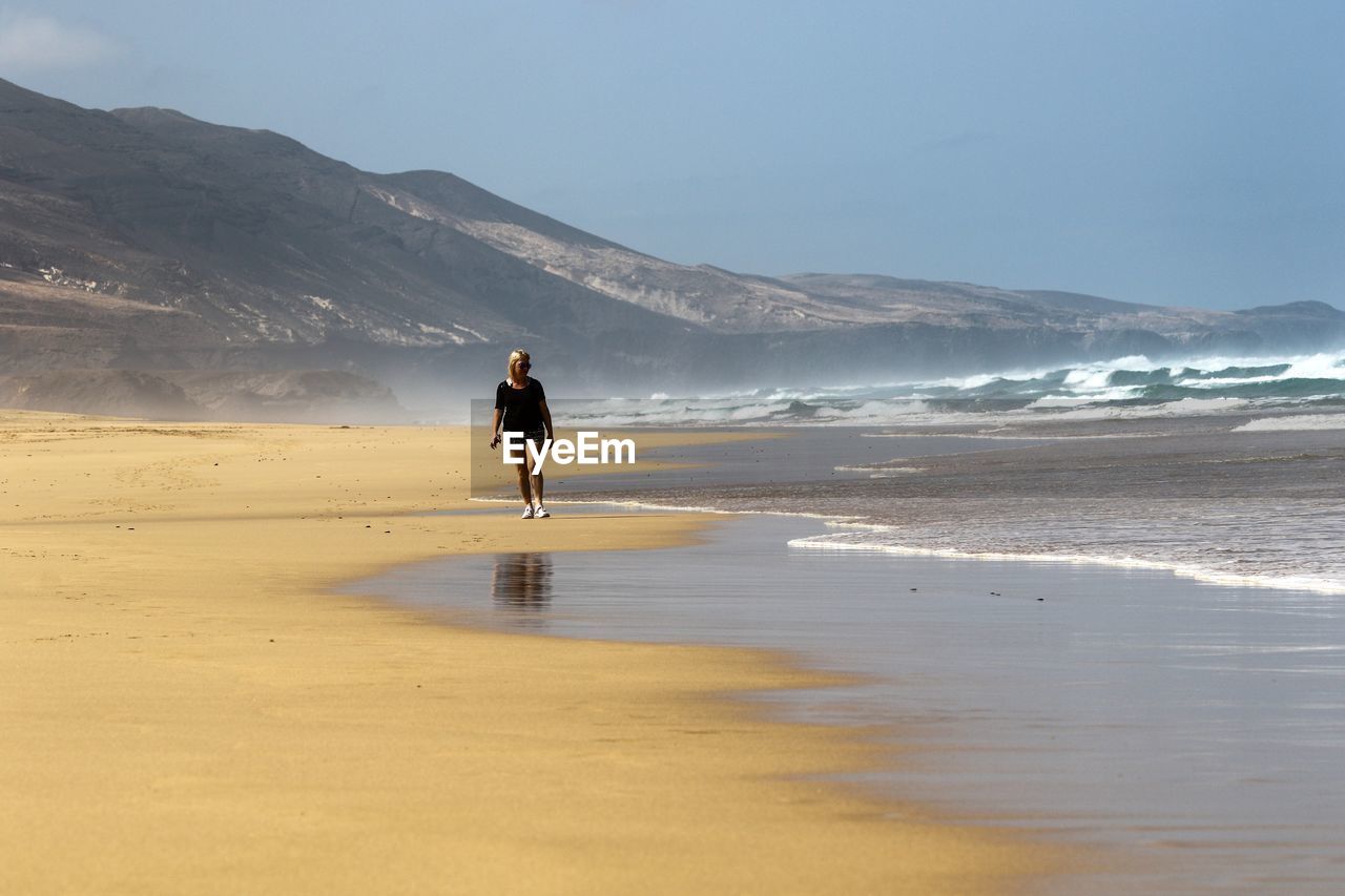Woman walking on beach against sky