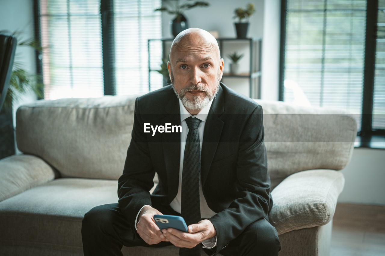 portrait of young man using mobile phone while sitting on sofa at home