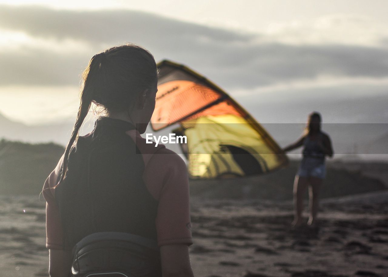 Friends with kite standing at beach against sky during sunset