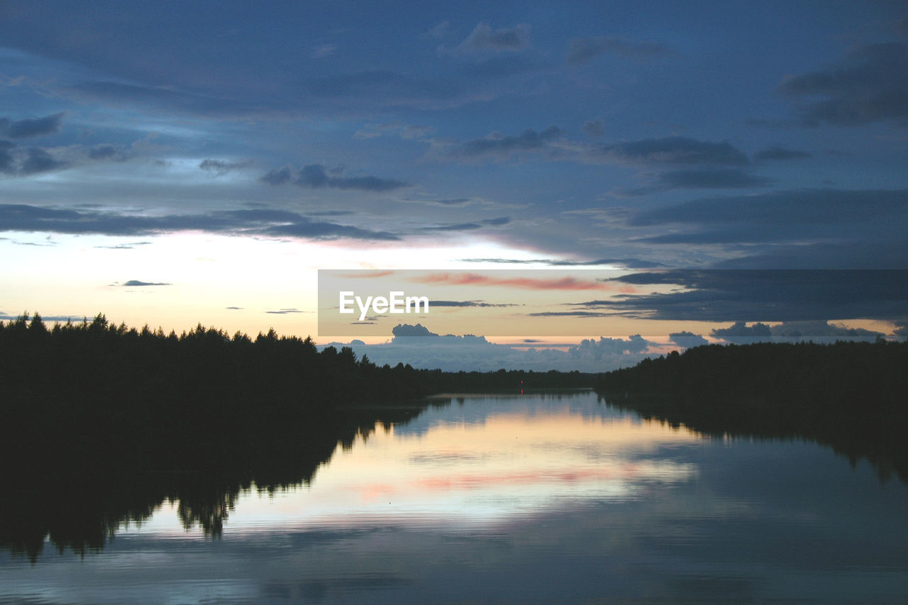 REFLECTION OF SILHOUETTE TREES IN LAKE AGAINST SKY DURING SUNSET