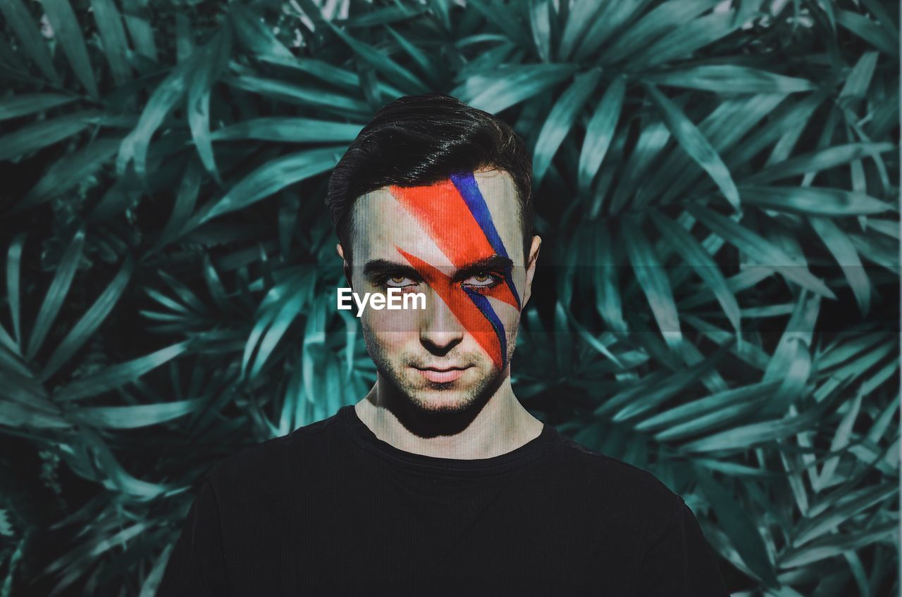 Portrait of young man with painted face standing against plants