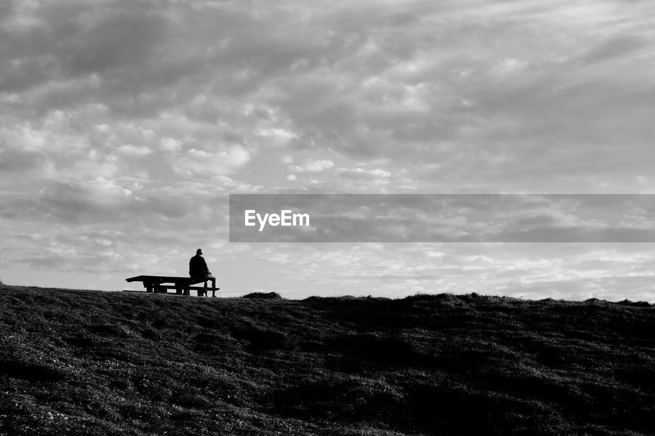 sky, horizon, cloud, black and white, monochrome, nature, silhouette, monochrome photography, one person, hill, sea, environment, landscape, sitting, leisure activity, black, coast, land, beauty in nature, adult, men, scenics - nature, outdoors, darkness, lifestyles, day, activity, tranquility, non-urban scene, full length, transportation, tranquil scene