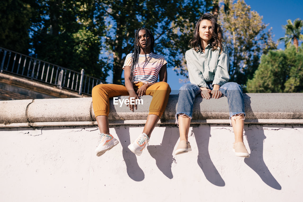 Low angle view of friends sitting on retaining wall