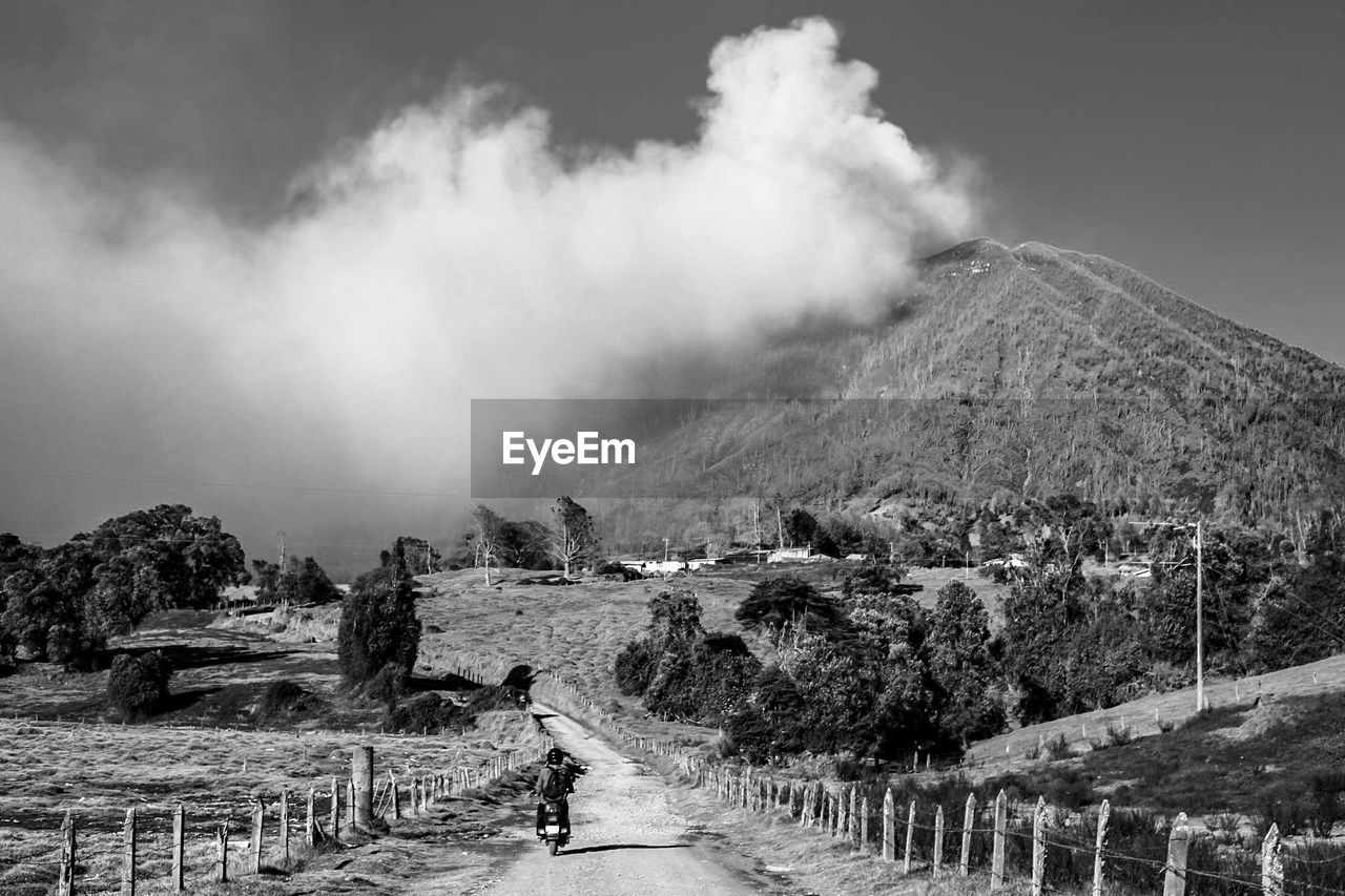 Rear view of person riding motorcycle on dirt road