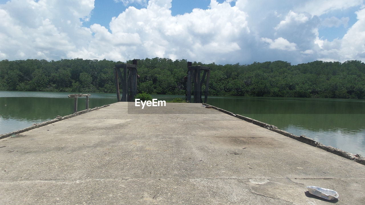 View along asphalt pier extending into calm lake