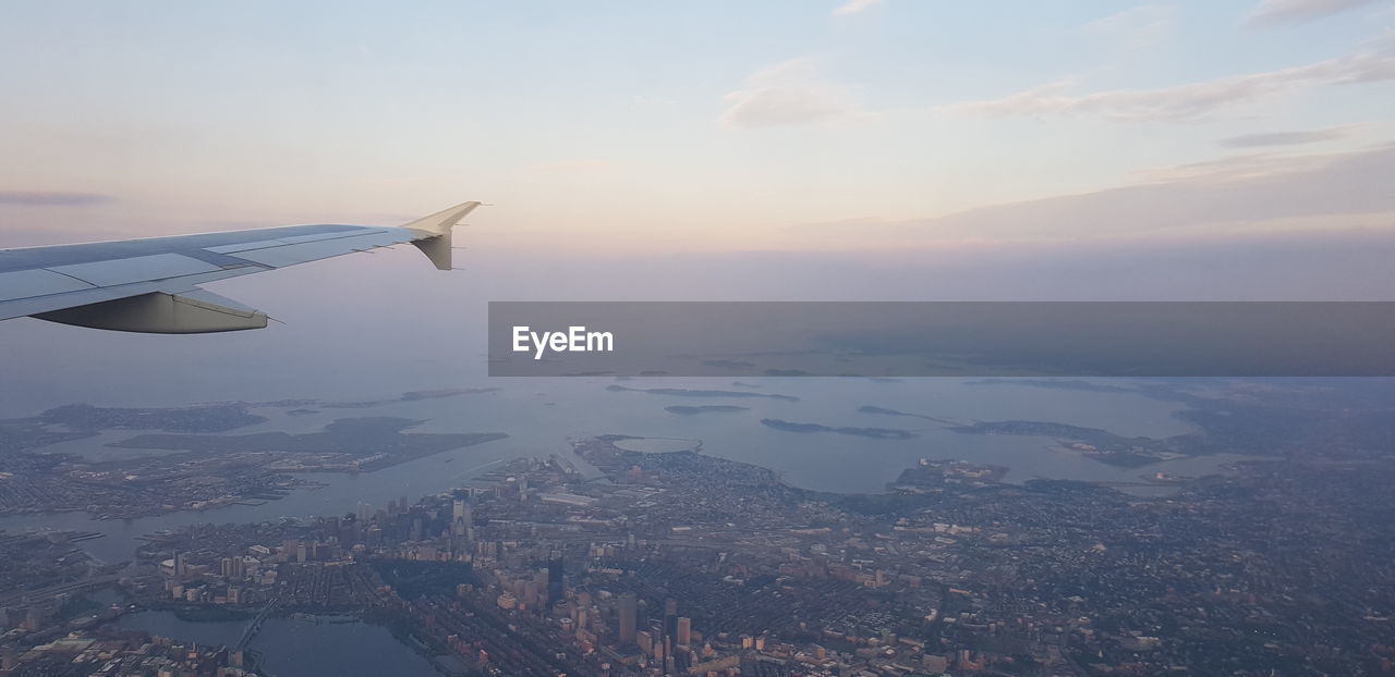 AERIAL VIEW OF AIRPLANE FLYING OVER CITYSCAPE DURING SUNSET