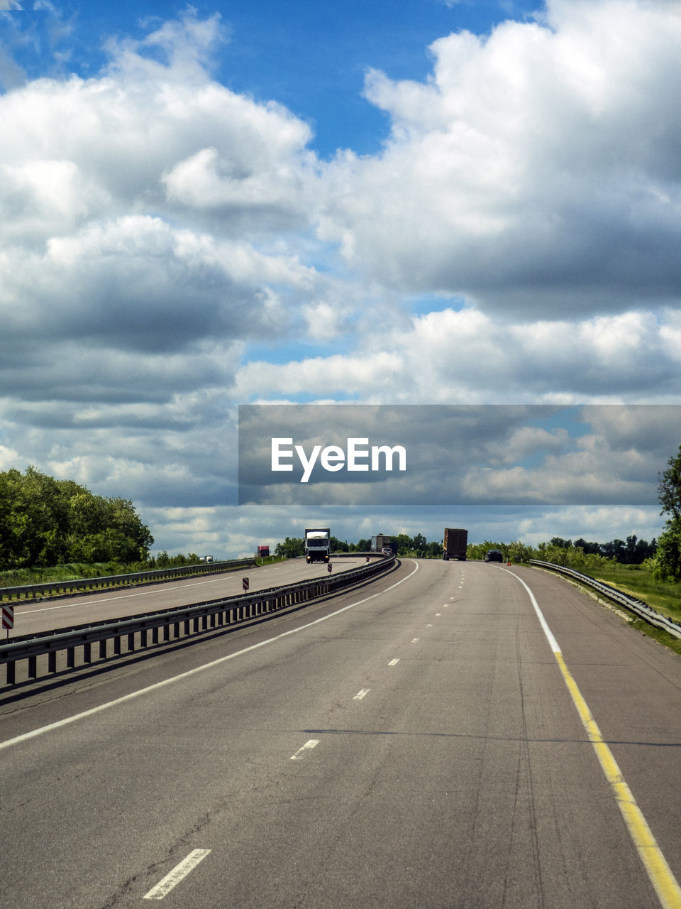 Trucks moving on highway against cloudy sky