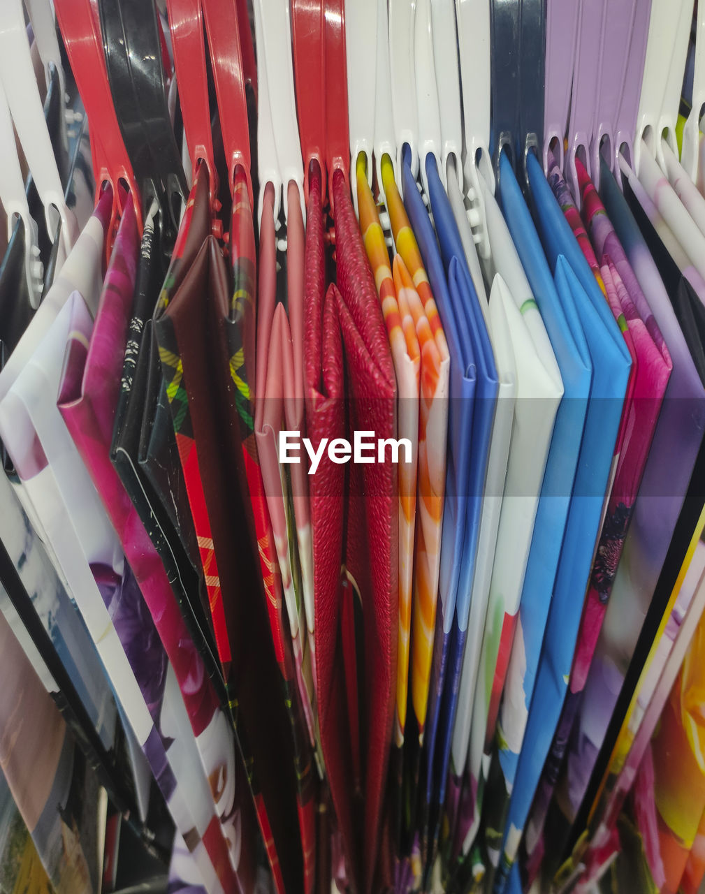 multi colored, large group of objects, variation, abundance, retail, no people, hanging, arrangement, in a row, store, indoors, clothing, fashion, still life, collection, business, order, shopping, for sale, rack, side by side, close-up