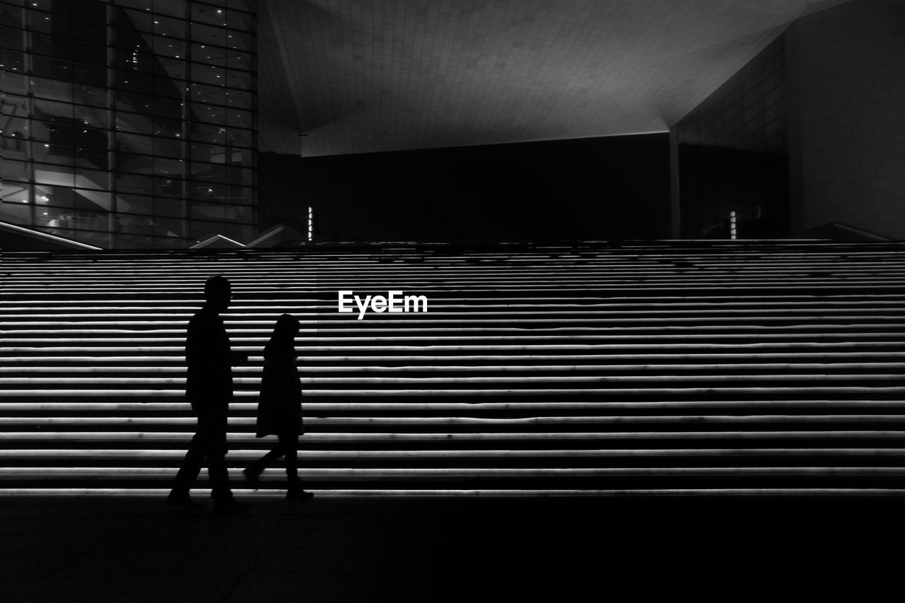 Silhouette man and woman walking on steps at night