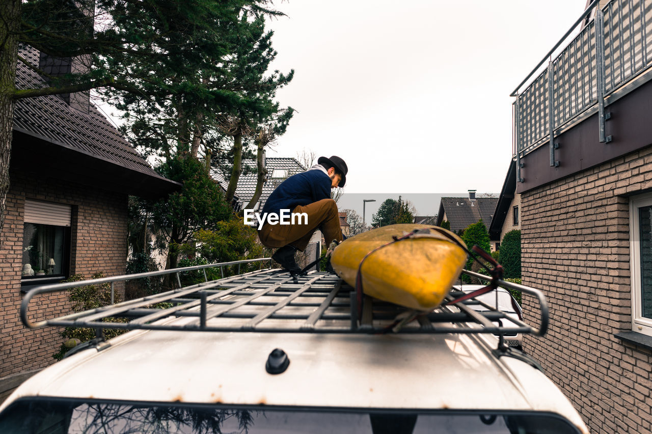 Young man crouching on car roof