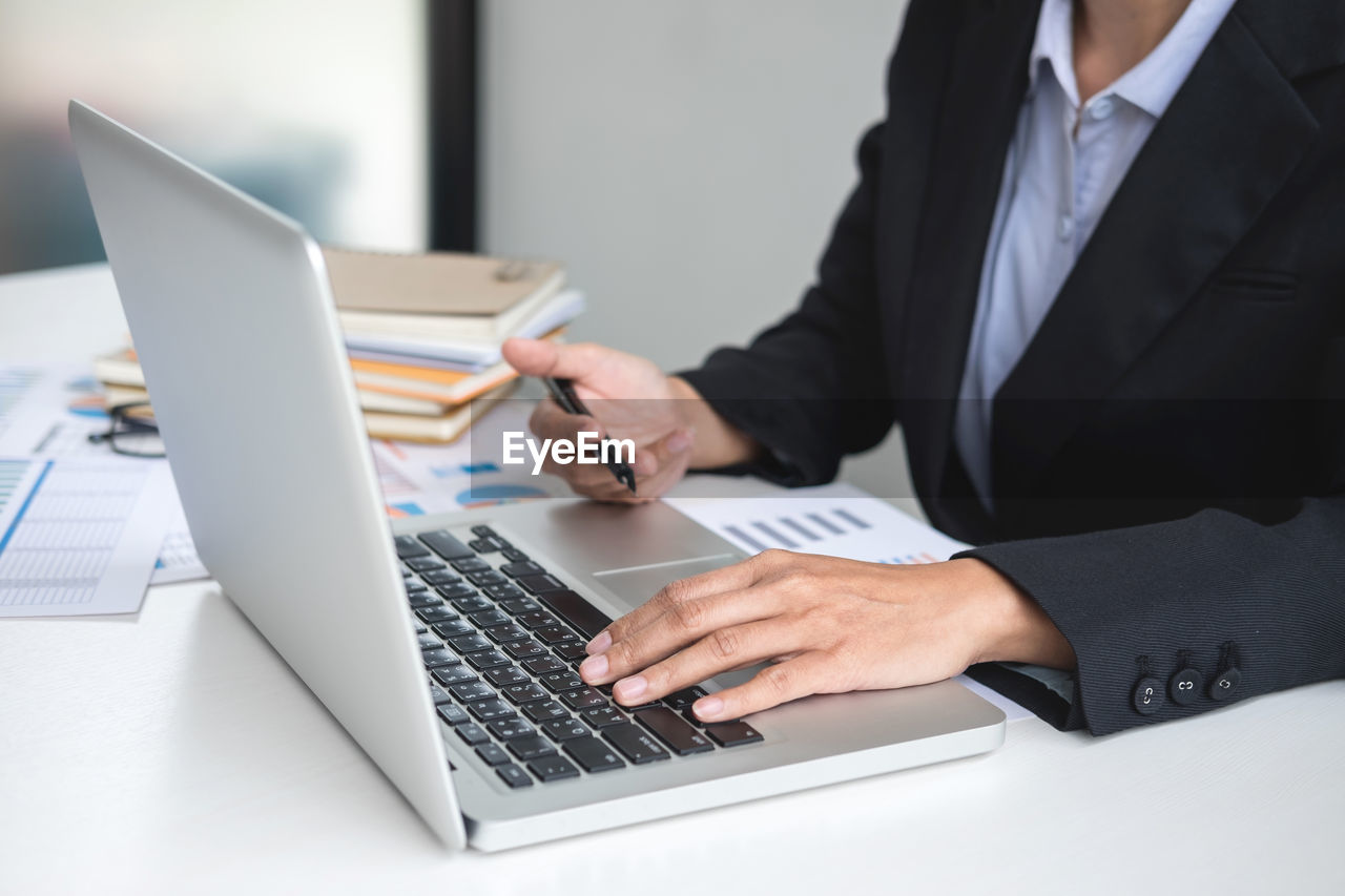 Midsection of businessman using laptop by graphs on table