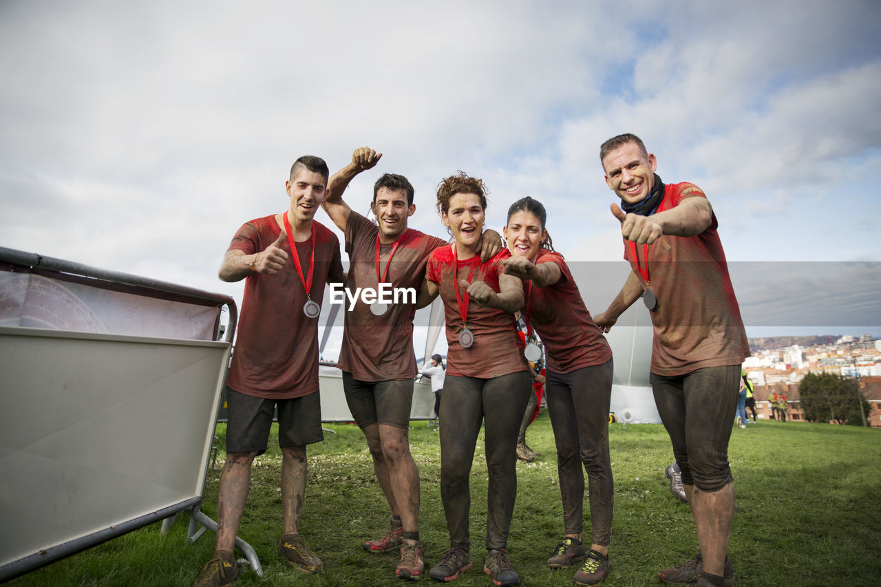 Portrait of team with medals celebrating success on field against sky