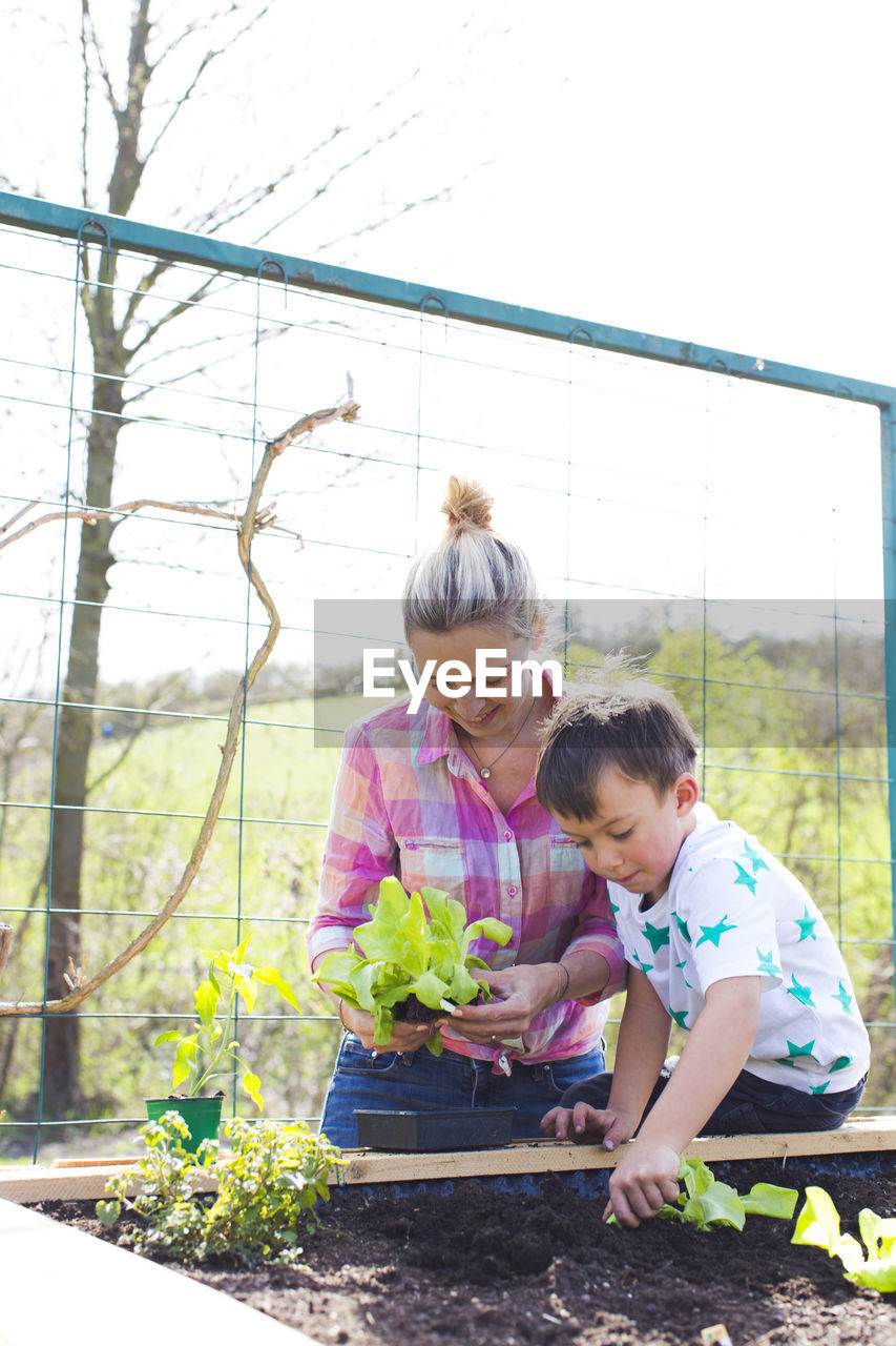 GIRL AND WOMAN STANDING BY PLANTS AGAINST WALL