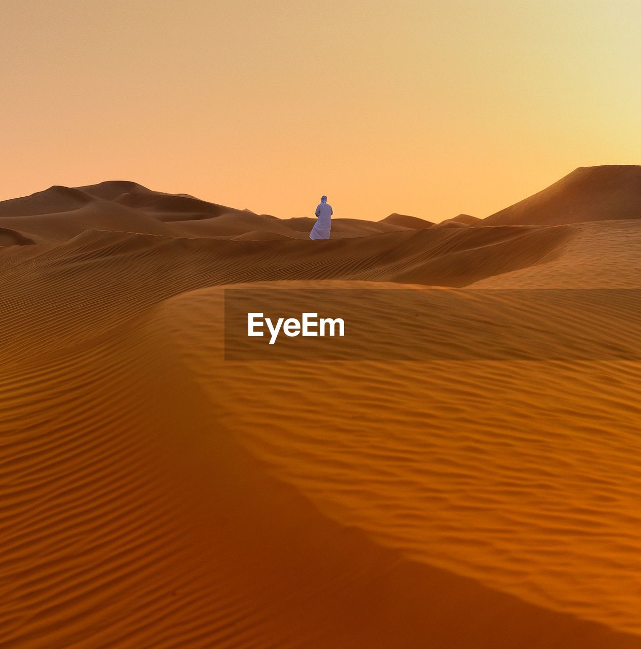 Rear view of person standing in desert against clear sky during sunset