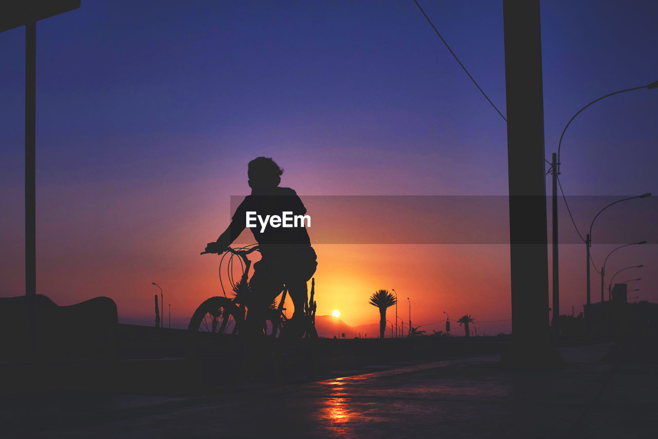 SILHOUETTE MAN RIDING BICYCLE ON STREET DURING SUNSET