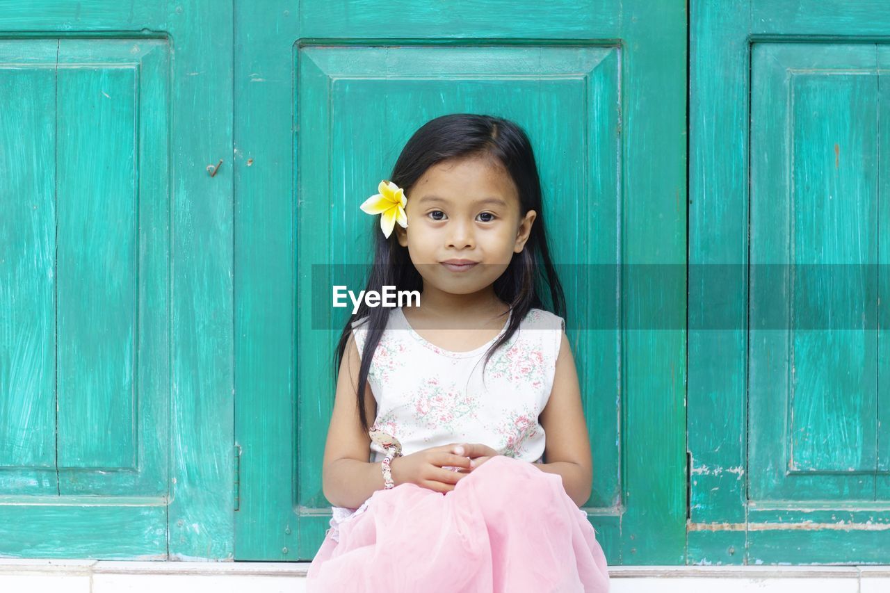 Portrait of cute girl wearing flower sitting against closed doors