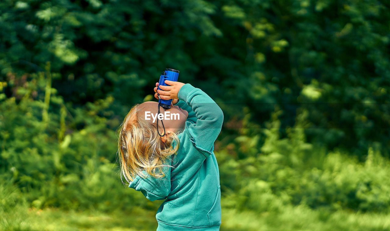 Side view of girl looking through binoculars while standing on land
