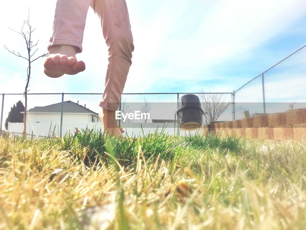 Low section of boy on grassy field against sky during sunny day