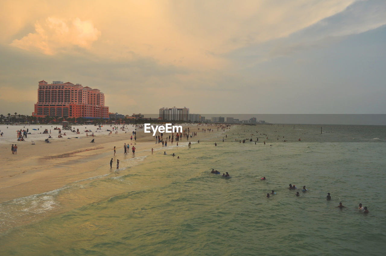 People enjoying at beach against sky during sunset