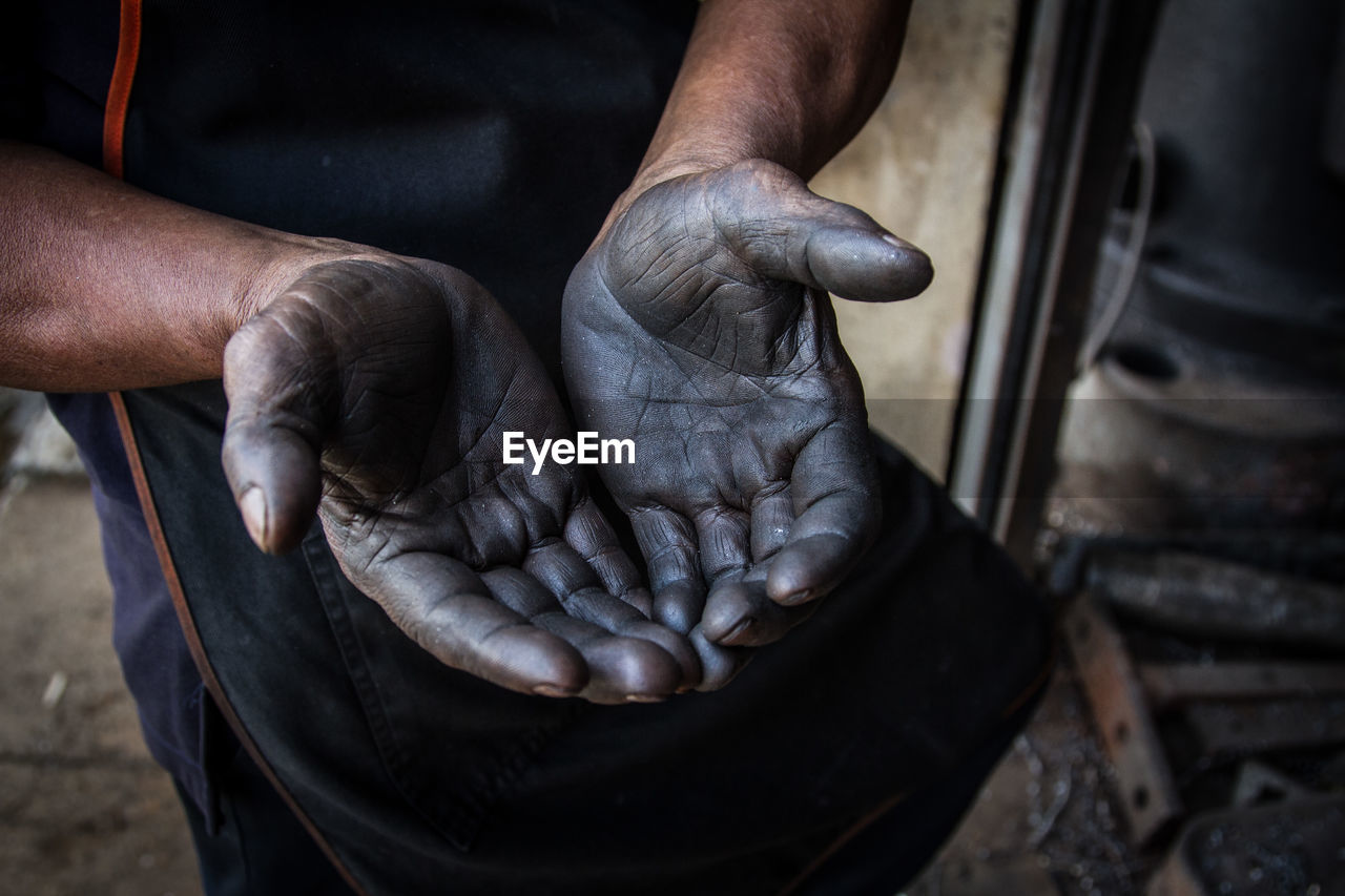 Midsection of manual worker showing dirty hands in factory