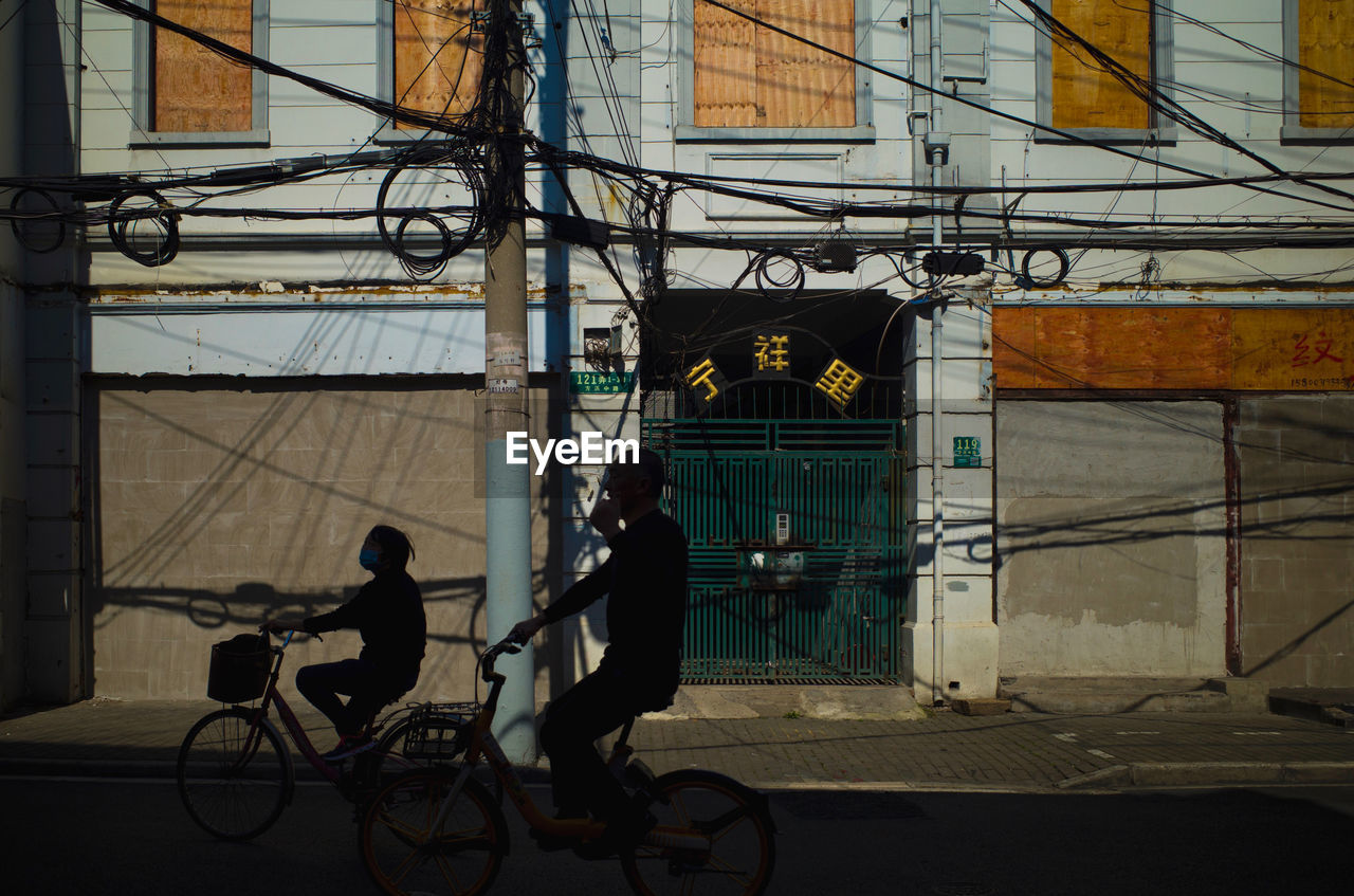 PEOPLE RIDING BICYCLE ON STREET AGAINST BUILDING