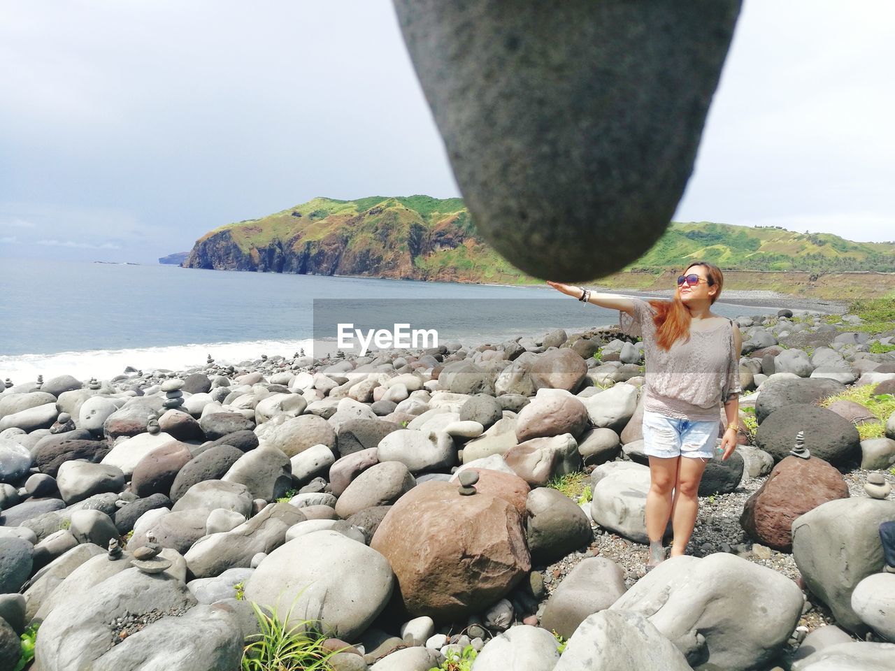 WOMAN STANDING ON ROCK BY SEA