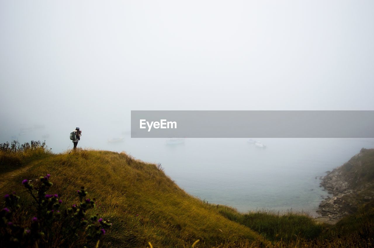 Woman standing on mountain against sky in foggy weather