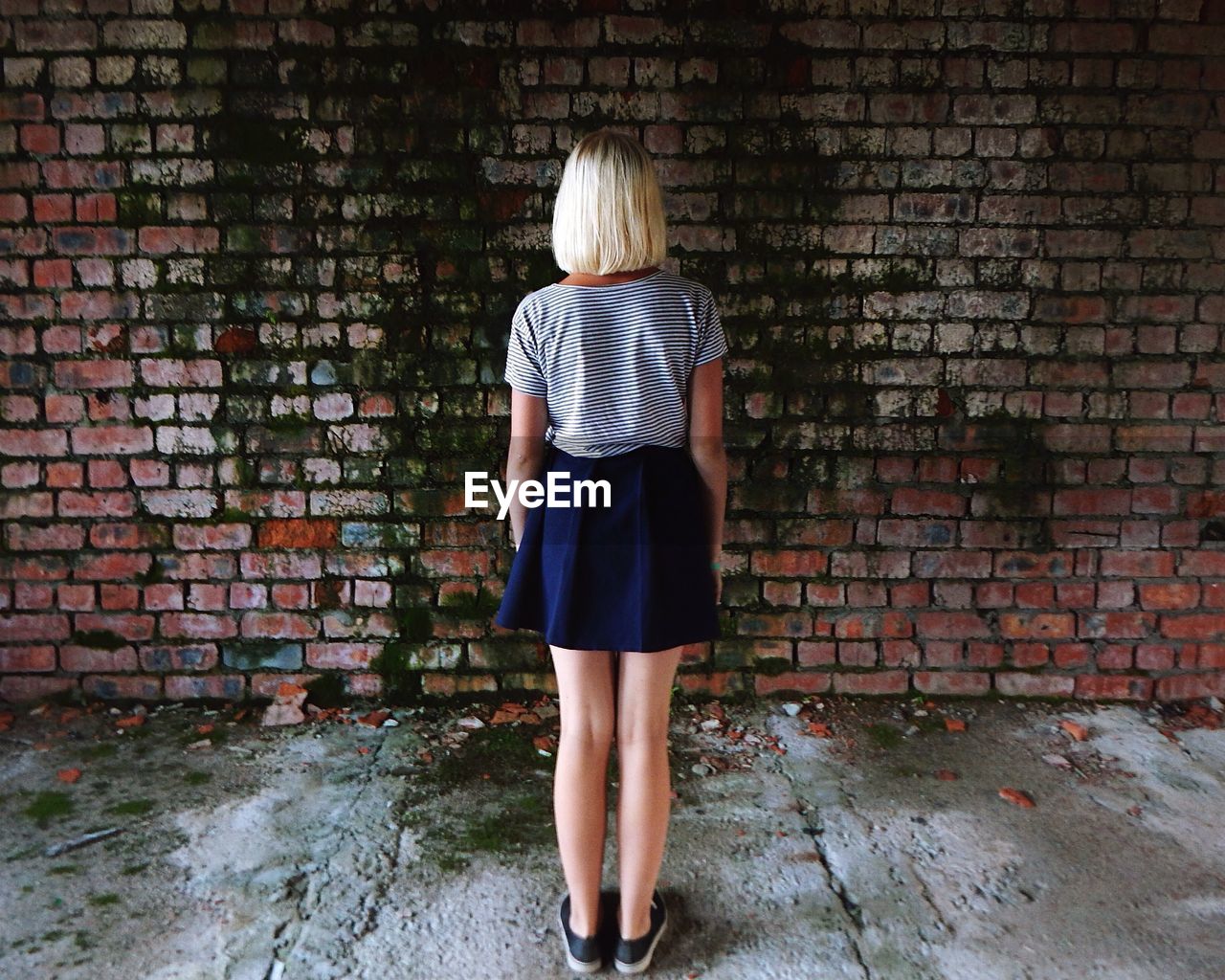 Rear view of girl standing against weathered brick wall in abandoned house