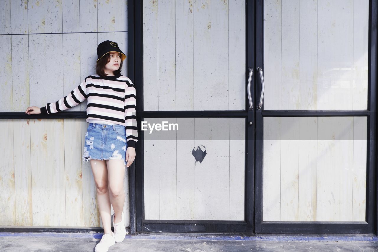 Portrait of young woman standing against wall