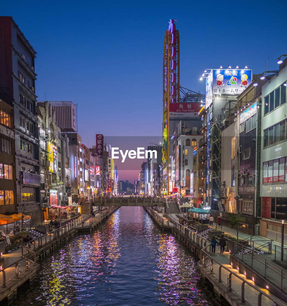 Canal amidst illuminated buildings in city during sunset