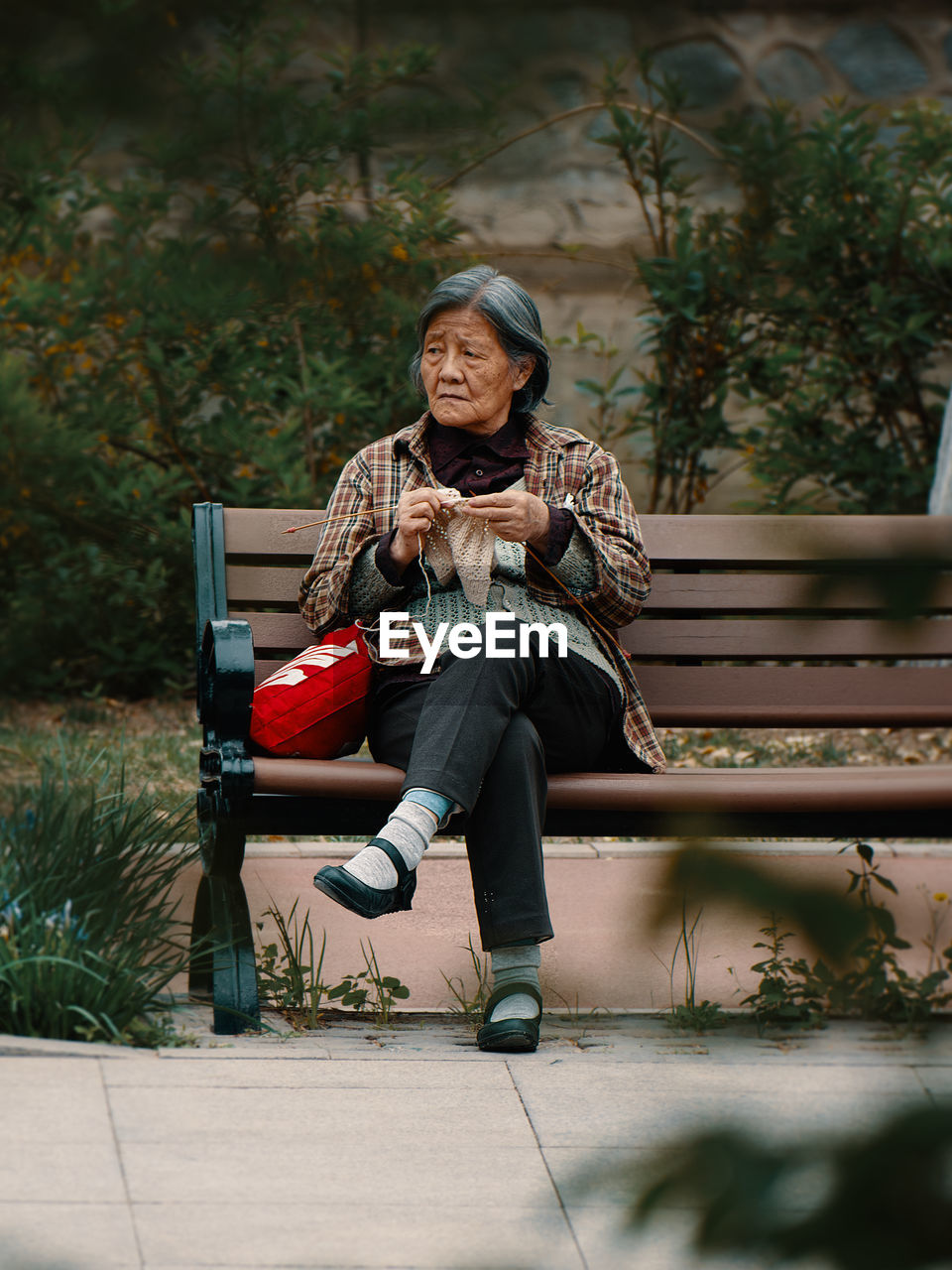 Elderly woman crocheting on a park bench