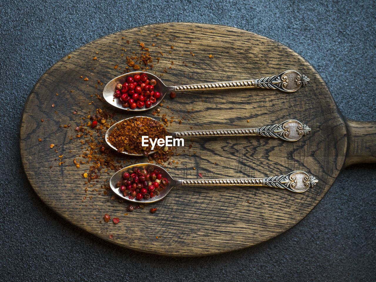 Close-up of chili flakes and dried fruits in spoons on wooden cutting board