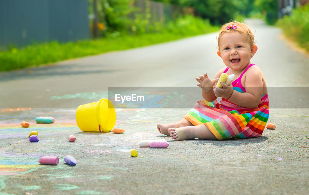 Cute baby girl playing with toy sitting on road