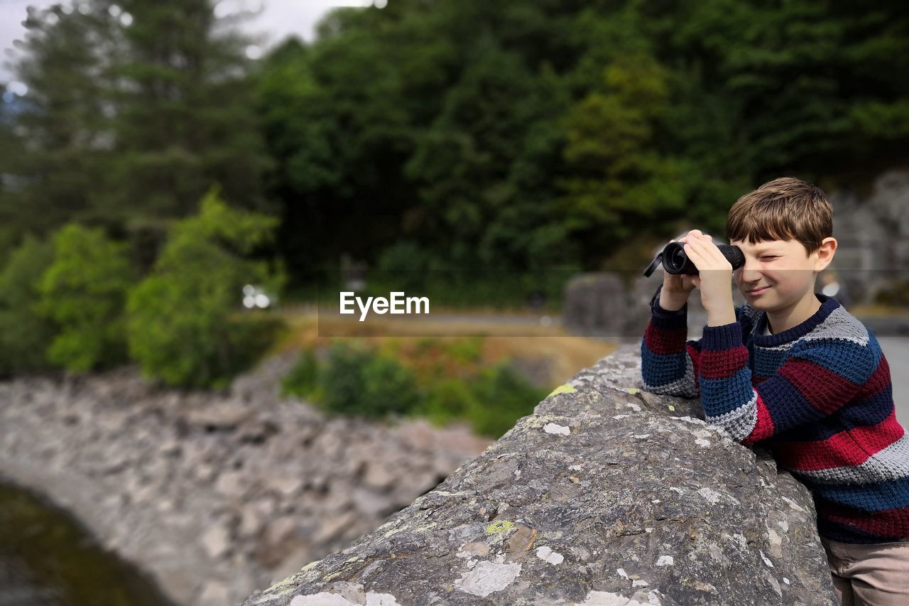 Boy looking through binoculars by retaining wall