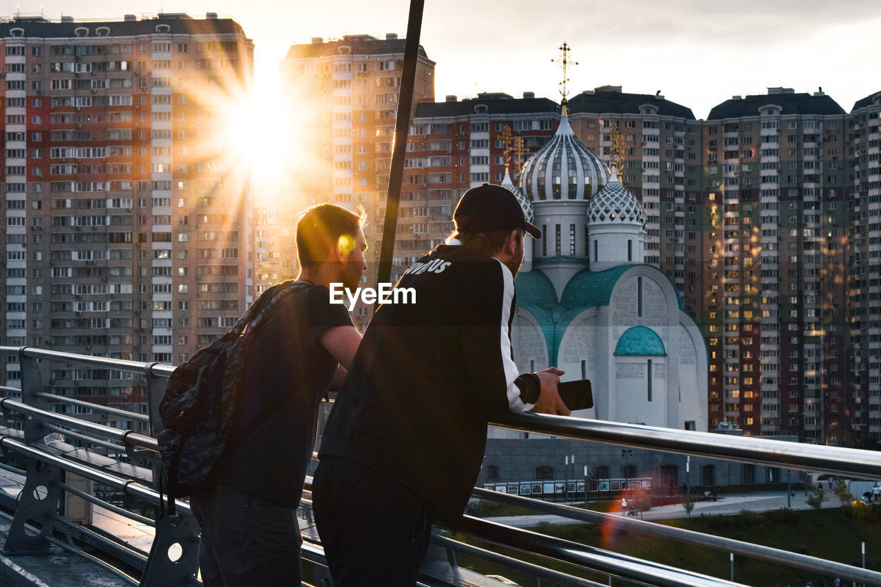 REAR VIEW OF PEOPLE STANDING IN CITY AGAINST BUILDINGS