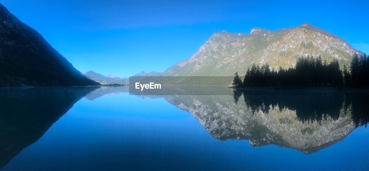 Scenic view of lake by mountains against clear blue sky