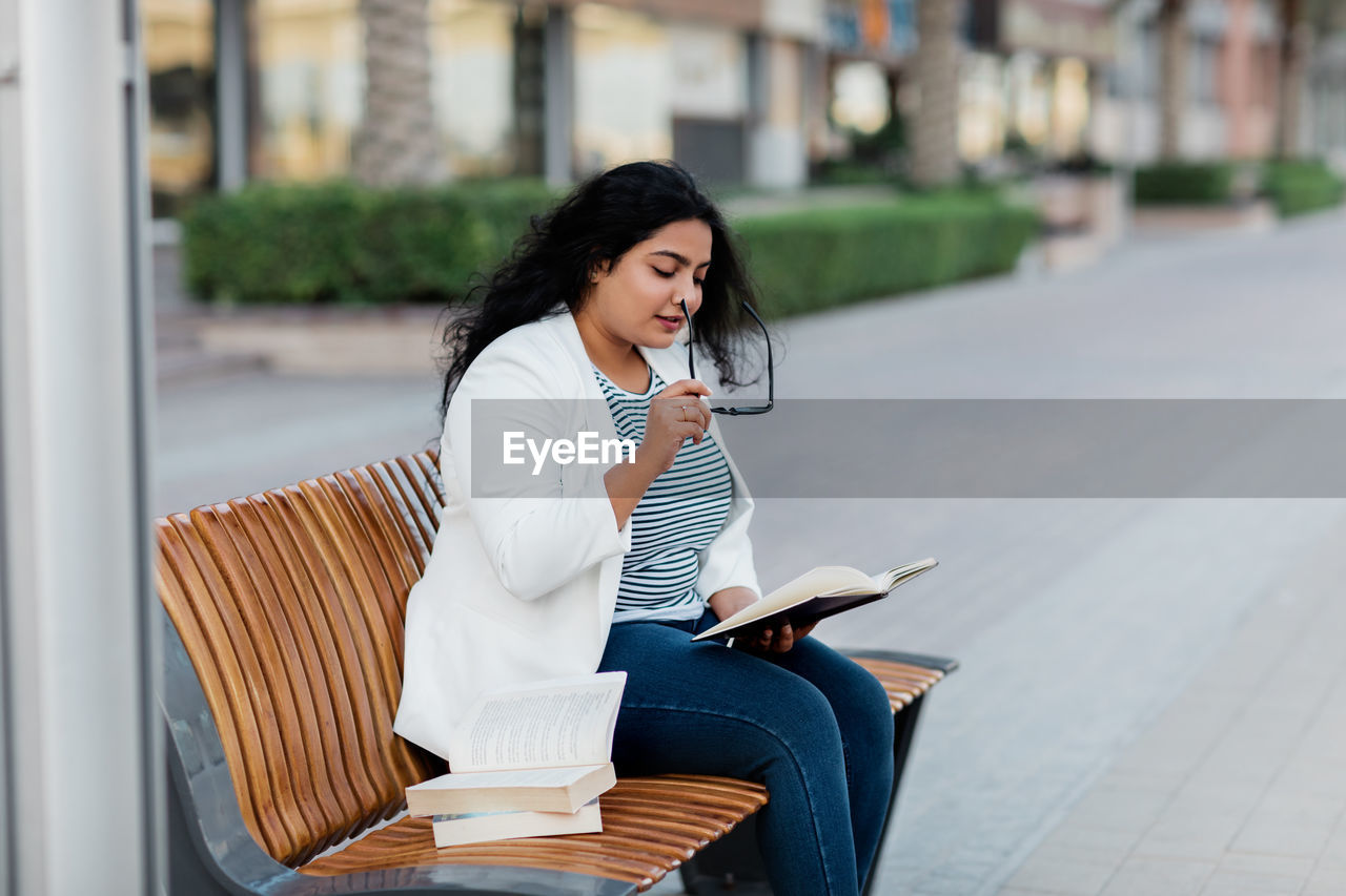A beautiful girl is sitting on a bench and reading a book. the concept of urban lifestyle 
