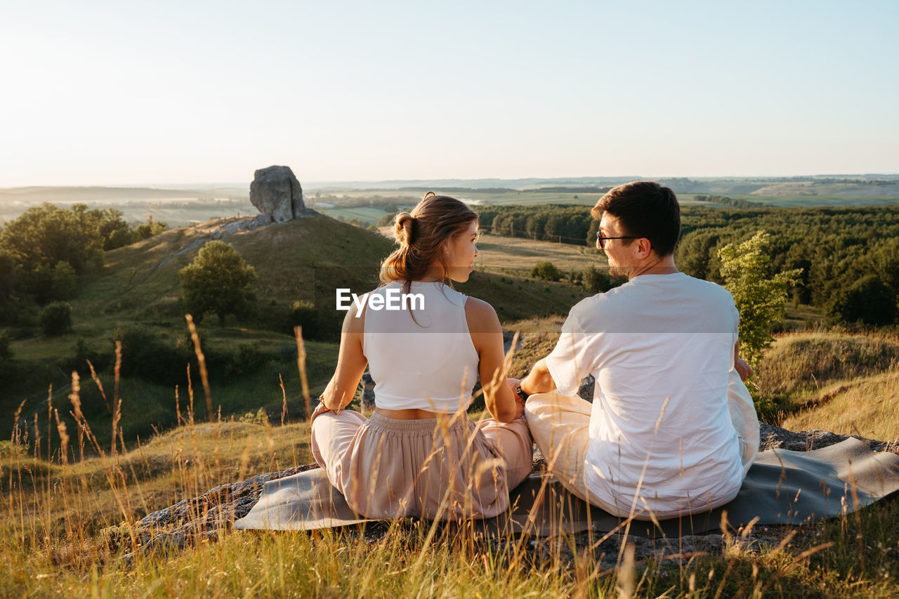 Man and woman practicing yoga and meditation outdoors at sunset with nature miracle giant stone