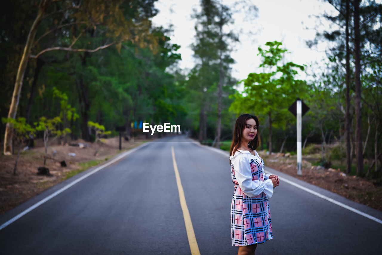 WOMAN STANDING ON ROAD AMIDST TREES