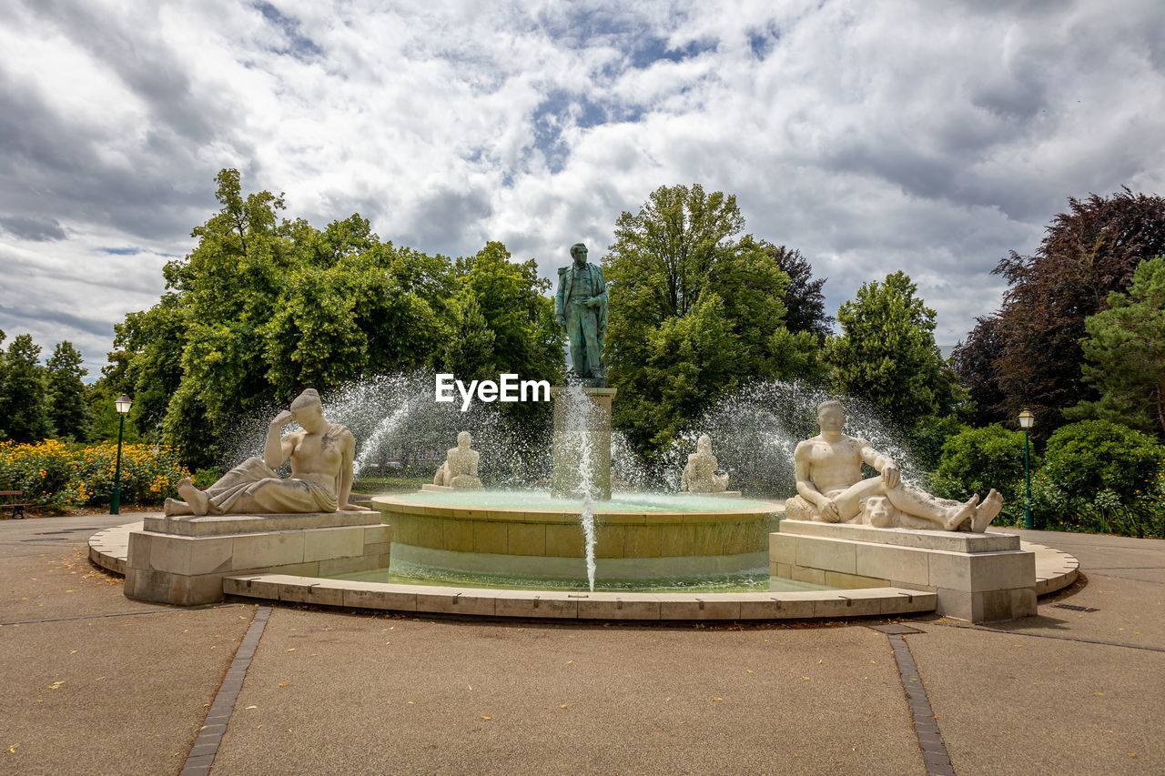 fountain, plant, tree, cloud, water, sky, nature, architecture, water feature, spraying, no people, sculpture, motion, reflecting pool, outdoors, day, park, park - man made space, memorial, estate, town square, garden, travel destinations, statue, built structure, formal garden, splashing