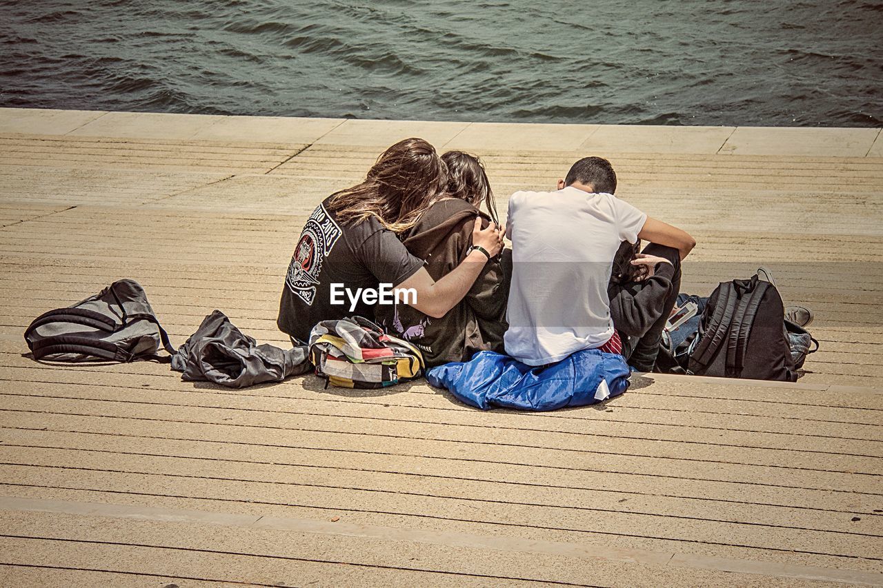 Rear view of couples sitting on pier at beach