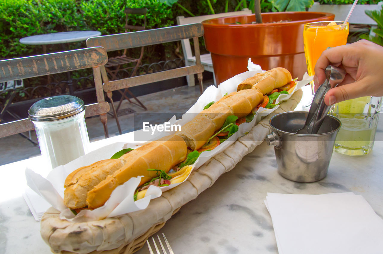 Cropped image of person holding serving tongs by sandwich on table