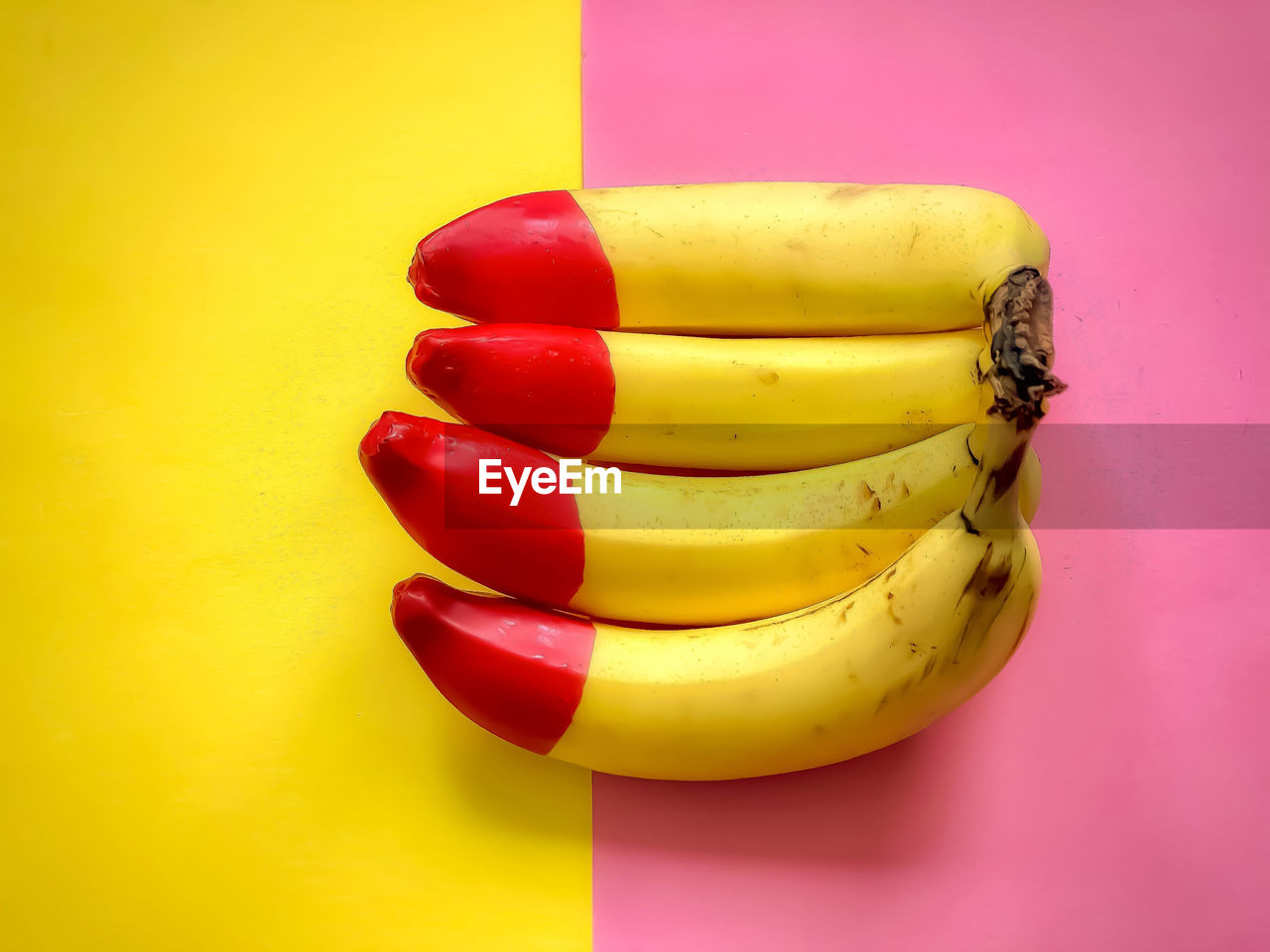 Close-up of red tipped bananas on yellow and pink background.