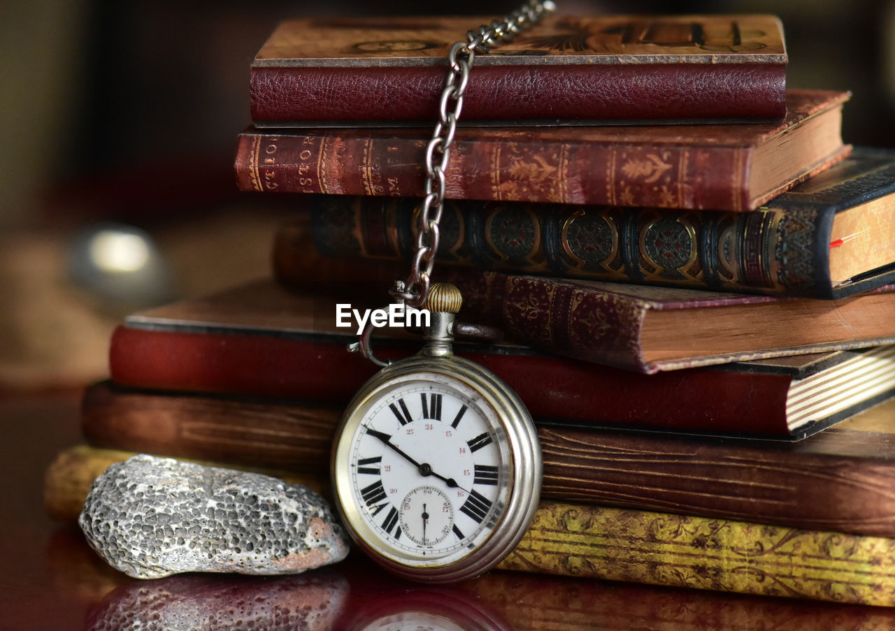 Close-up of pocket watch against old books on table